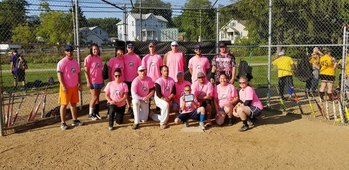 A team in matching pink shirts with their plaque at home plate